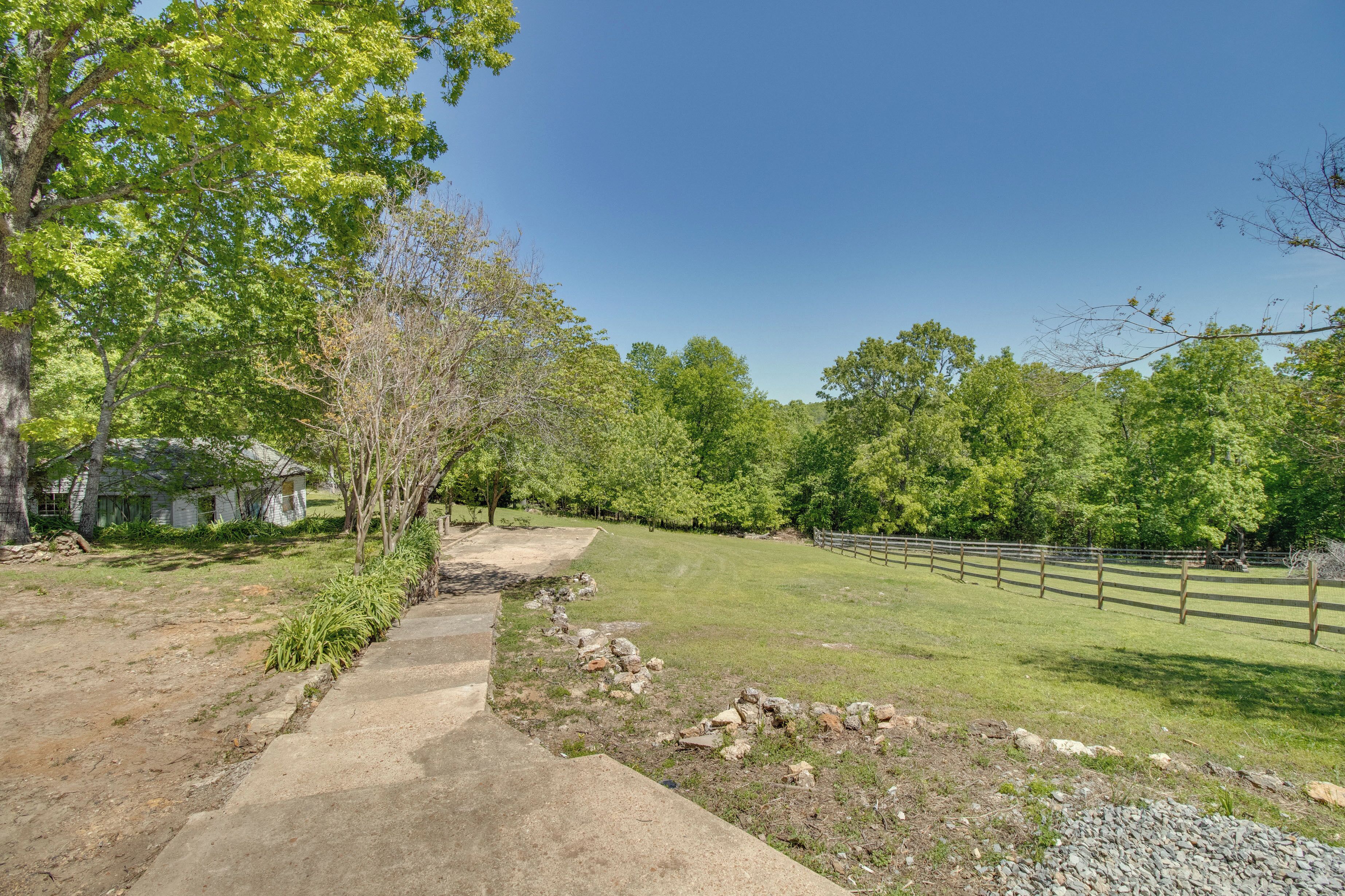A concrete pathway leading to a grassy area with a wooden fence and trees.