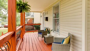 A wooden porch with wicker furniture and a bench, a brick house in the background, and a car parked on the street. - Walkable Apt Near Kentucky Derby! (Louisville)