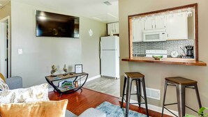 A modern living room with a flat-screen TV, a dining area with stools, and a kitchen with white cabinets and a microwave. - Walkable Apt Near Kentucky Derby! (Louisville)