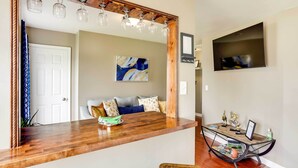 A modern living room with a wooden coffee table, a sofa with patterned cushions, a mounted TV, and a decorative mirror with hanging lights. - Walkable Apt Near Kentucky Derby! (Louisville)