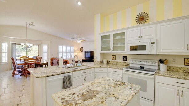 A kitchen with white cabinets, a granite countertop, a stove, and a dining area with wooden chairs and a table. - 55+ Gilbert Home w/ Yard, Golf Course On-site (Gilbert)