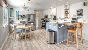 Une cuisine moderne avec des meubles blancs, un îlot central et un coin repas doté de chaises en bois.
