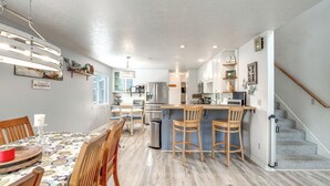 Une cuisine moderne avec un îlot central, des chaises en bois et une table à manger recouverte d’une nappe colorée.