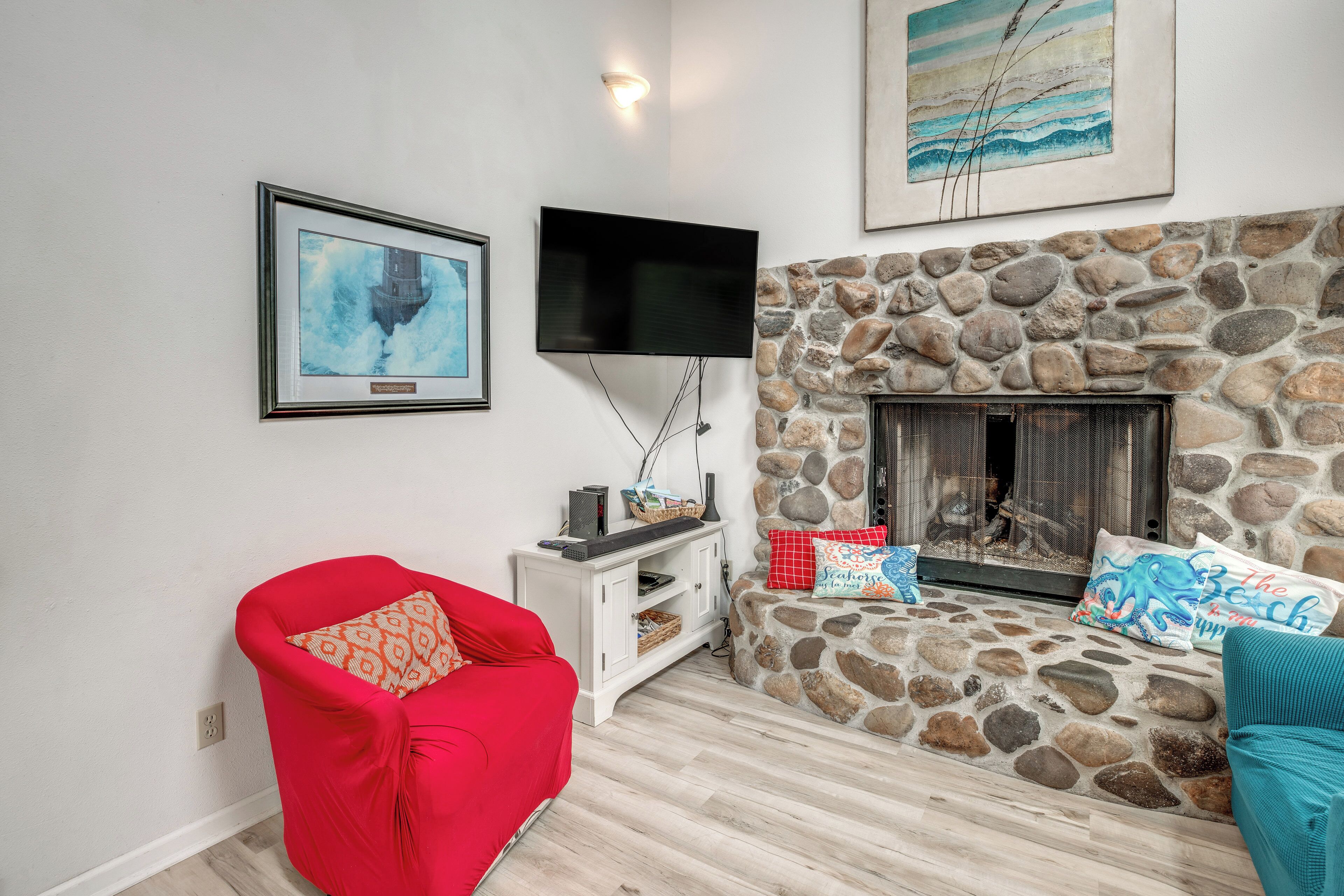 A living room with a stone fireplace, a mounted TV, and a red armchair.
