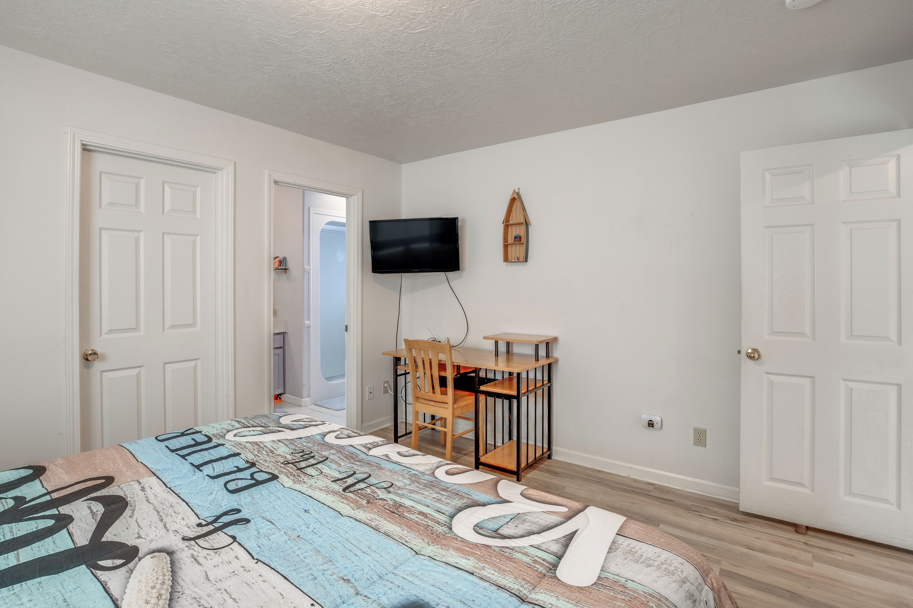 A bedroom with a bed, a desk, a chair, a television, and a door.