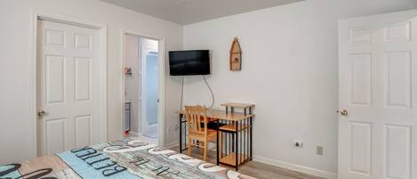A bedroom with a bed, a desk, a chair, a television, and a door.