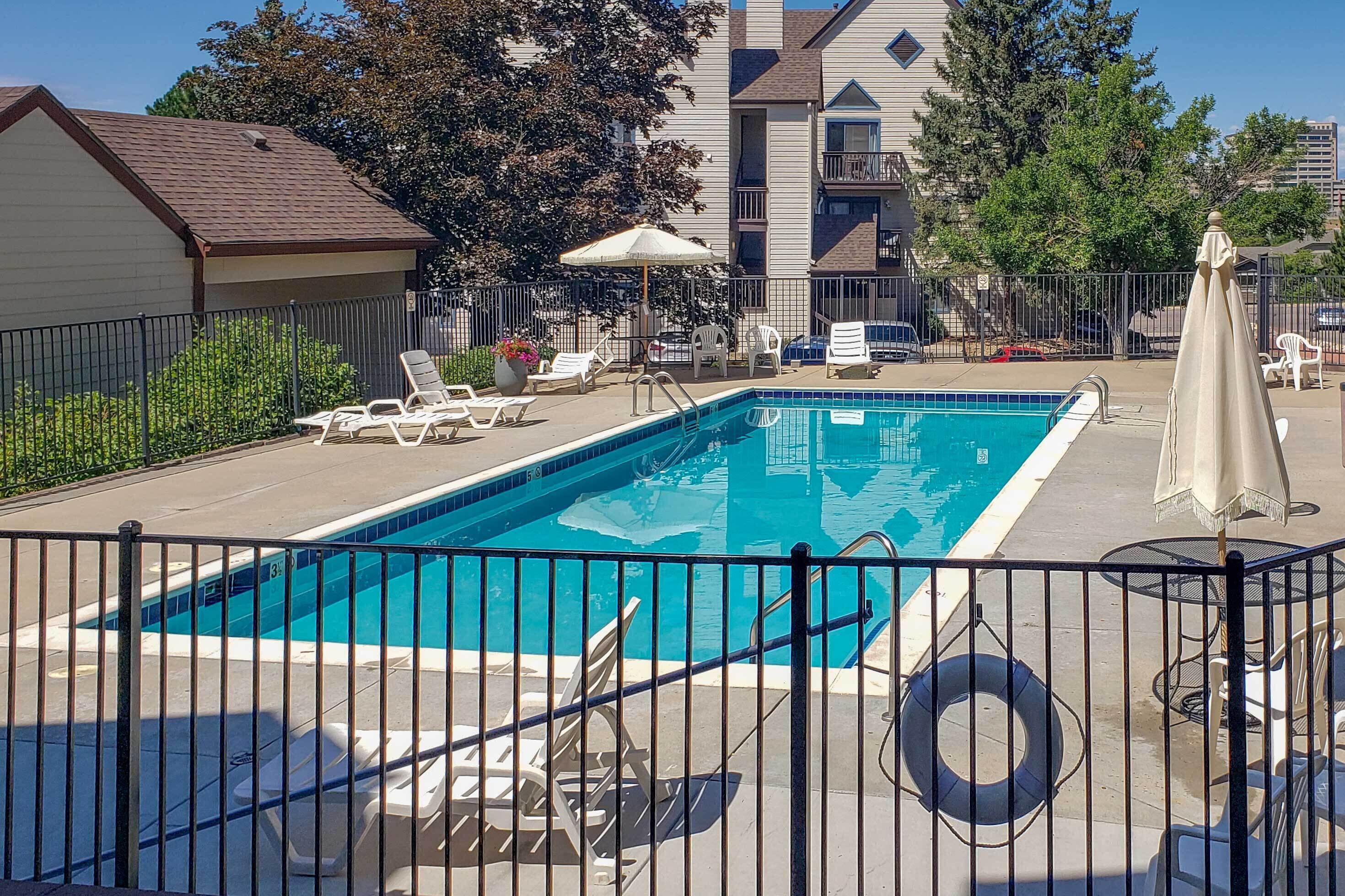 Ein rechteckiger Swimmingpool mit Metallzaun, umgeben von Liegestühlen und Sonnenschirmen.