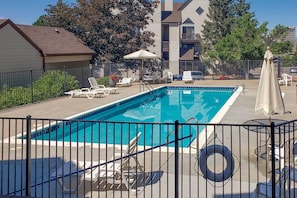 A rectangular swimming pool with a metal fence, surrounded by lounge chairs and umbrellas.