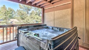 Un bain à remous sur une terrasse en bois, avec vue sur les arbres et un bâtiment en arrière-plan.