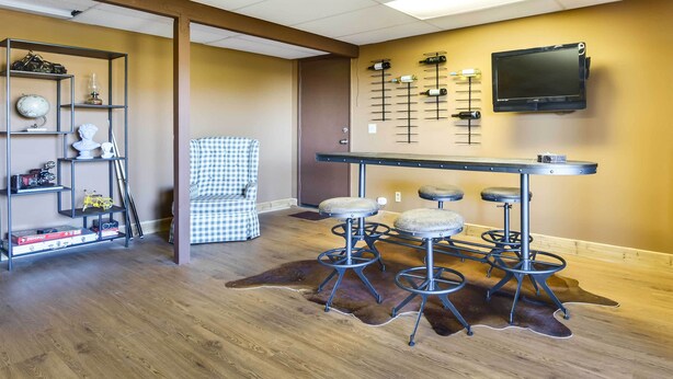 Un coin bar avec des tabourets, un téléviseur fixé au mur et une étagère contenant divers objets.