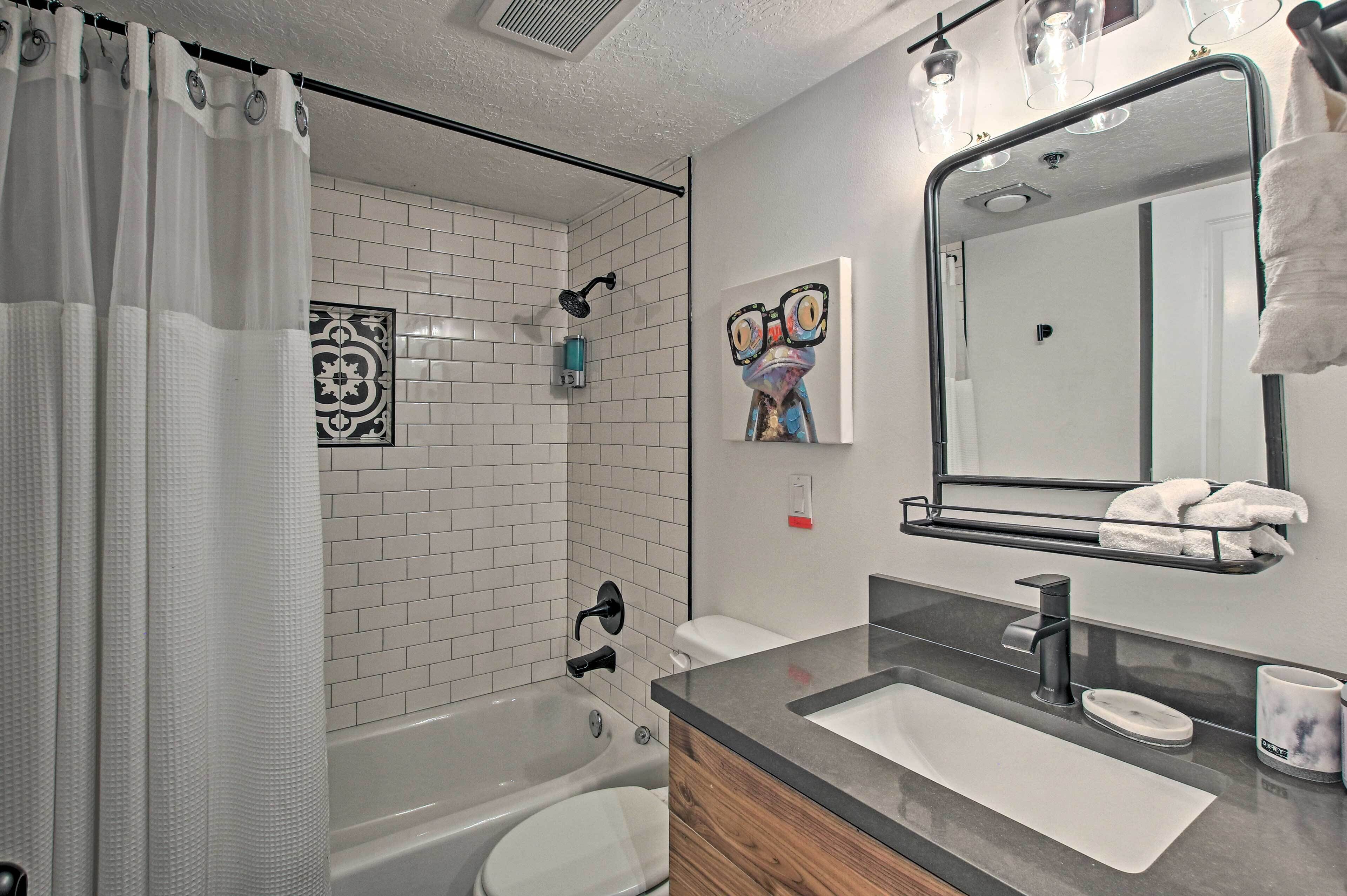 A modern bathroom with a bathtub, toilet, and sink. There is a shower curtain, a towel rack, and a mirror with a towel hanging on it.
