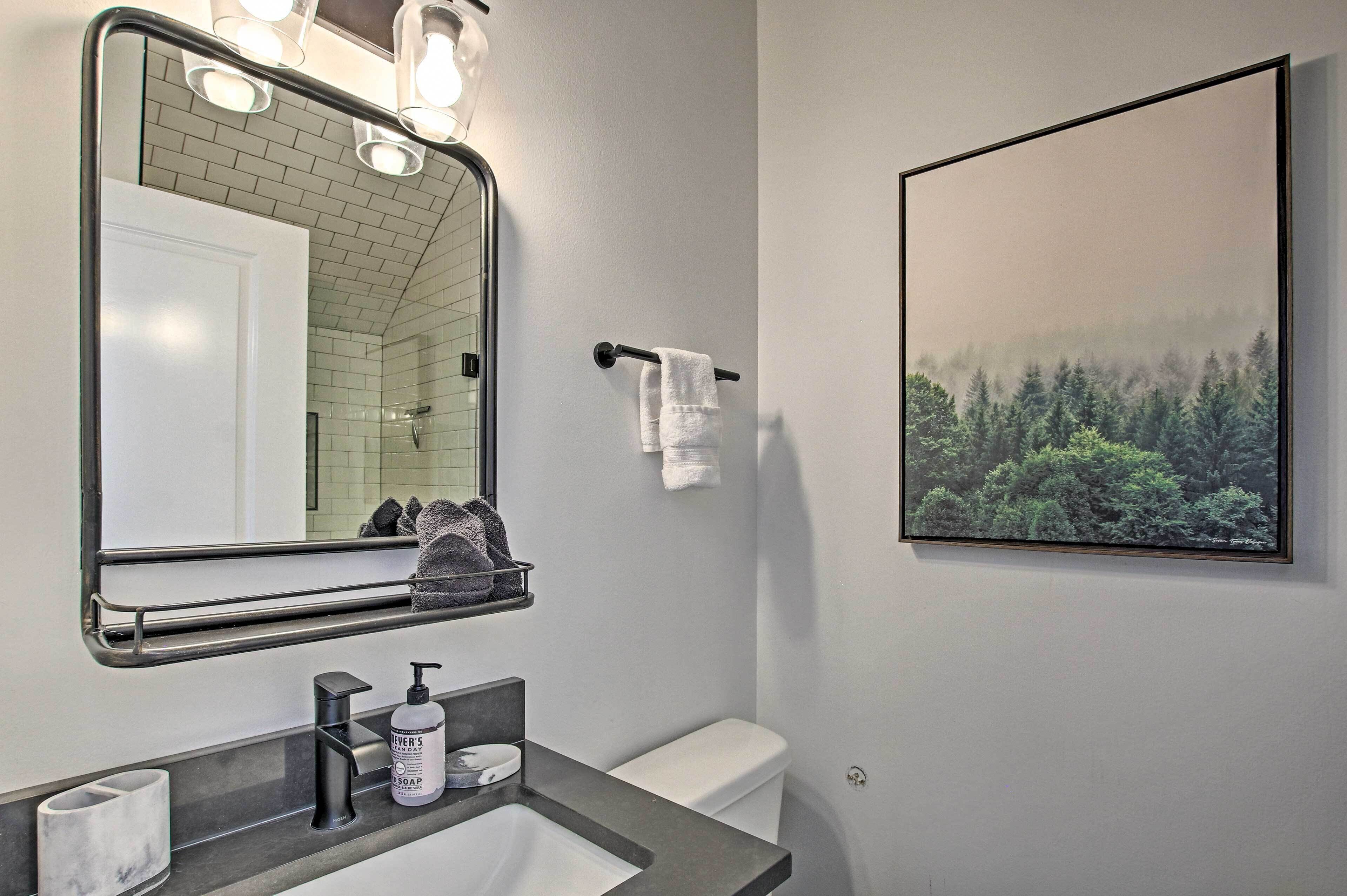 A bathroom with a large mirror, a towel rack, a sink with a soap dispenser, and a framed picture on the wall.