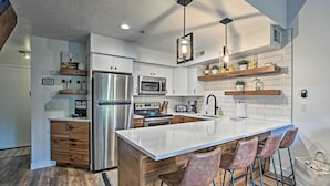 Una cocina moderna con una isla central, electrodomésticos de acero inoxidable, armarios de madera y taburetes de bar.
