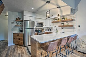 A modern kitchen with a central island, stainless steel appliances, wooden cabinetry, and bar stools.