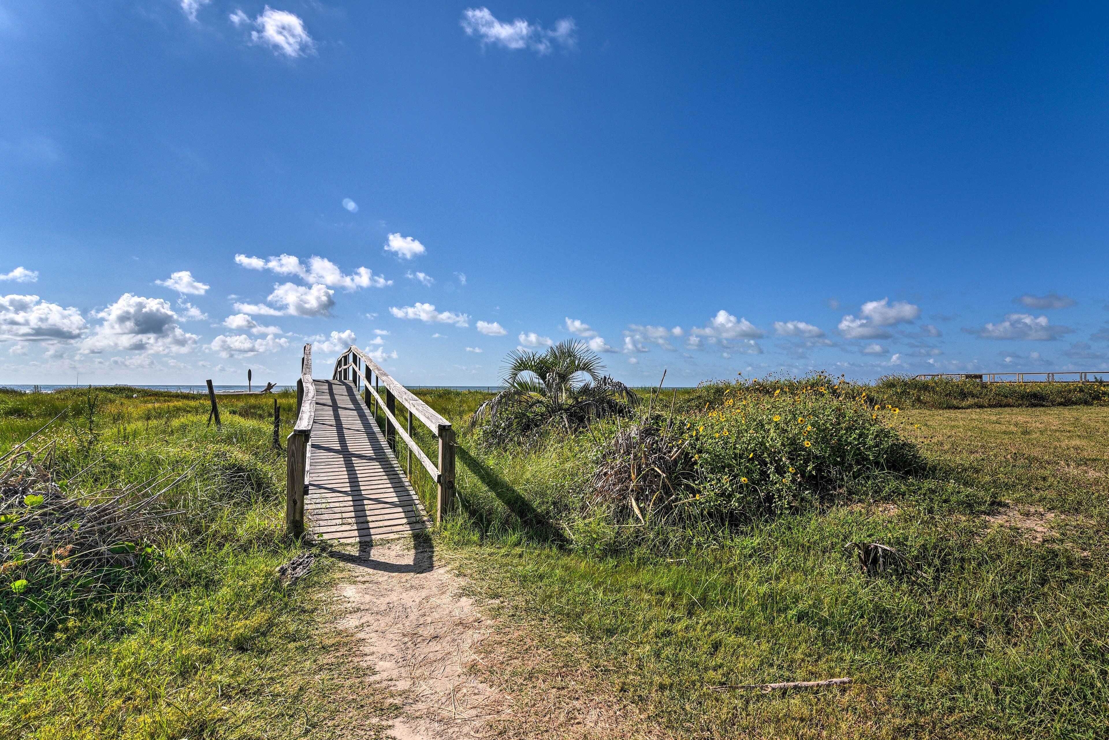 A wooden boardwalk leading to a beach with a clear sky and distant horizon.