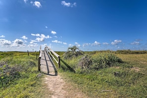 A wooden boardwalk leading to a beach with a clear sky and distant horizon.