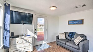 Un salon avec un canapé gris, un téléviseur à écran plat fixé au mur, une commode blanche et un plancher en bois.