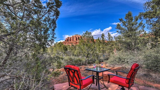 Une terrasse avec deux chaises rouges et une table, d’où l’on peut admirer un paysage montagneux.