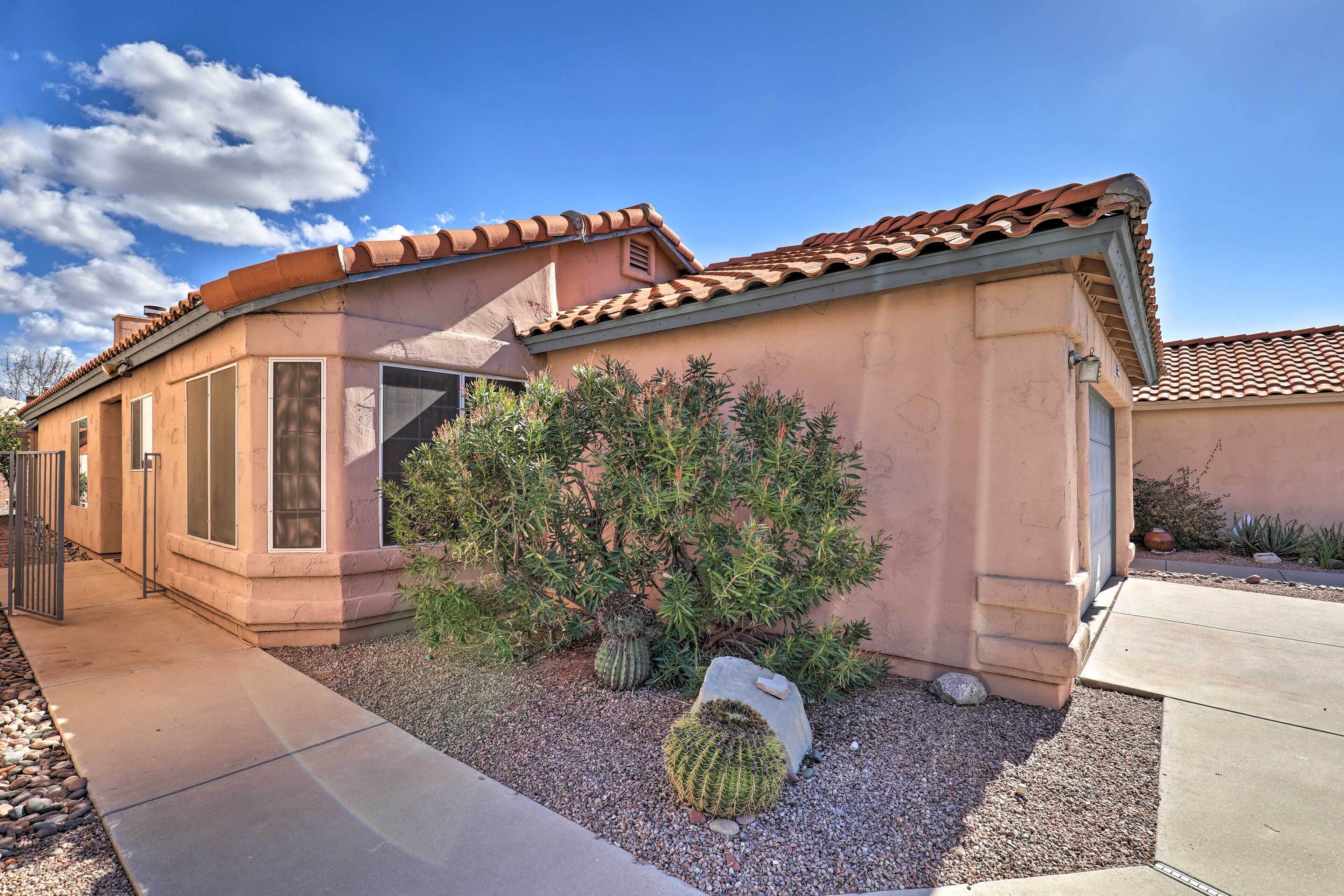 A house with a curved roof, large windows, and a well-maintained garden with cacti and a rock.