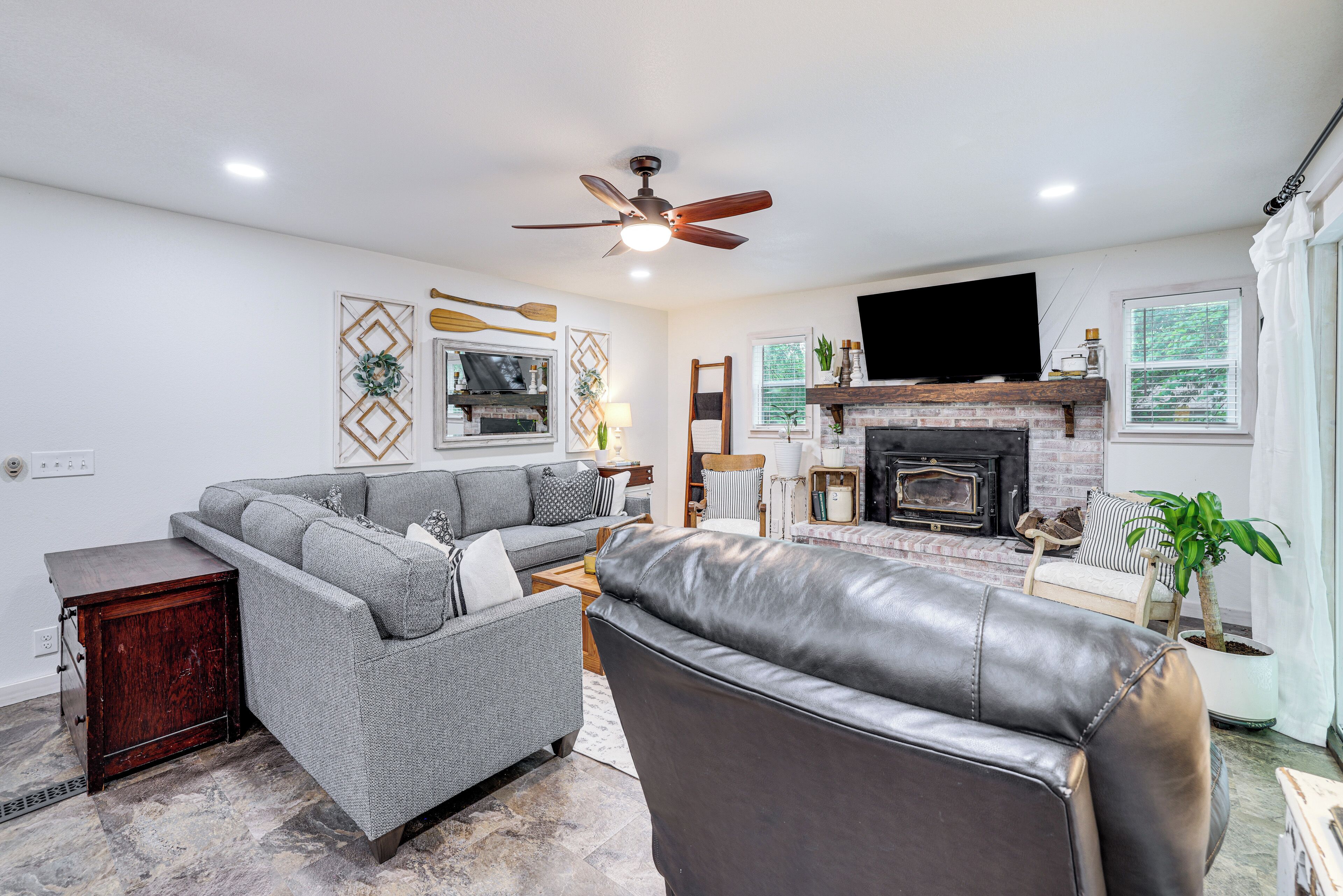 A living room with a fireplace, a sofa, a leather chair, and a ceiling fan.