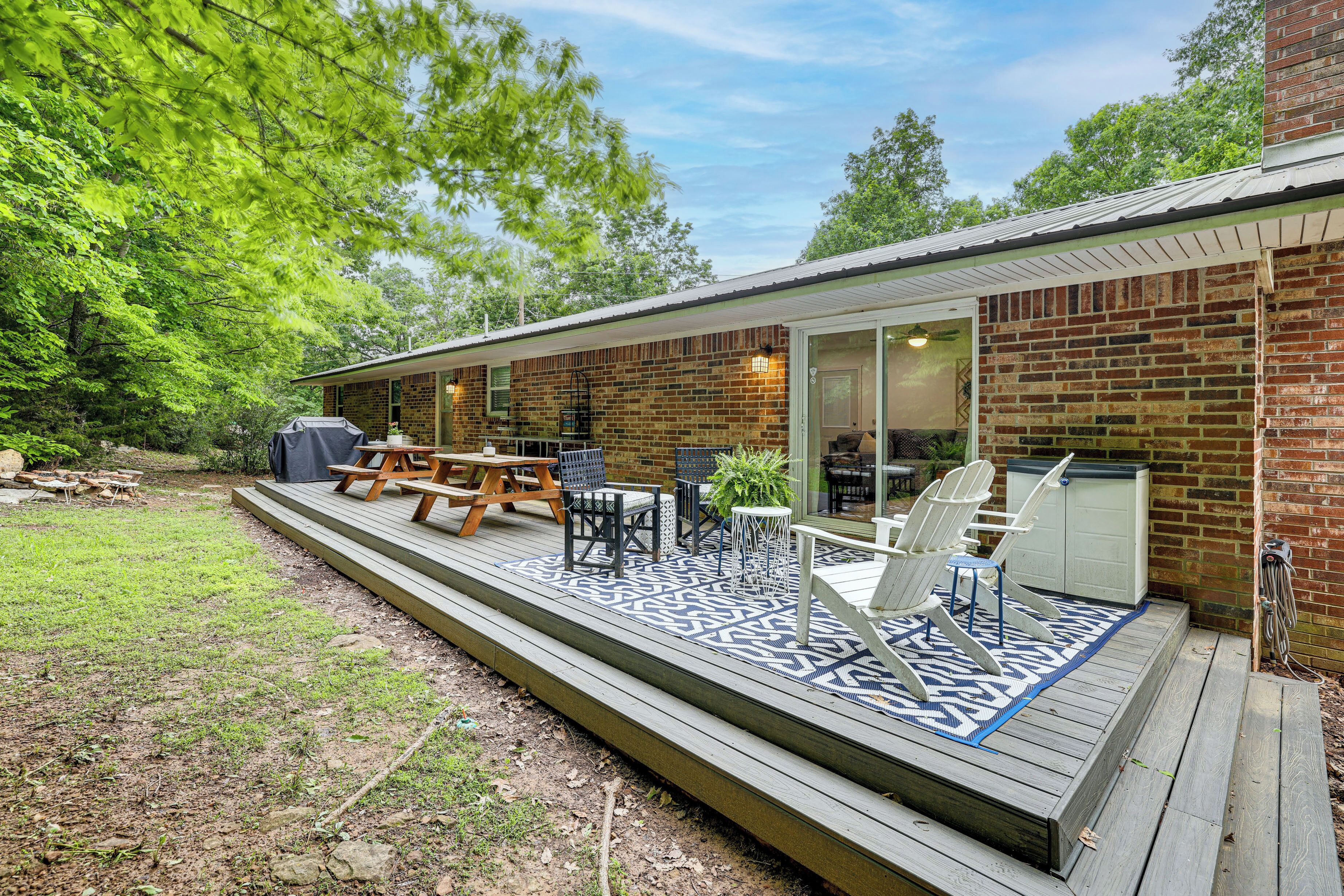 Eine überdachte Terrasse mit Gartenmöbeln, einem Grill und einem Backsteinhaus mit Glastür.