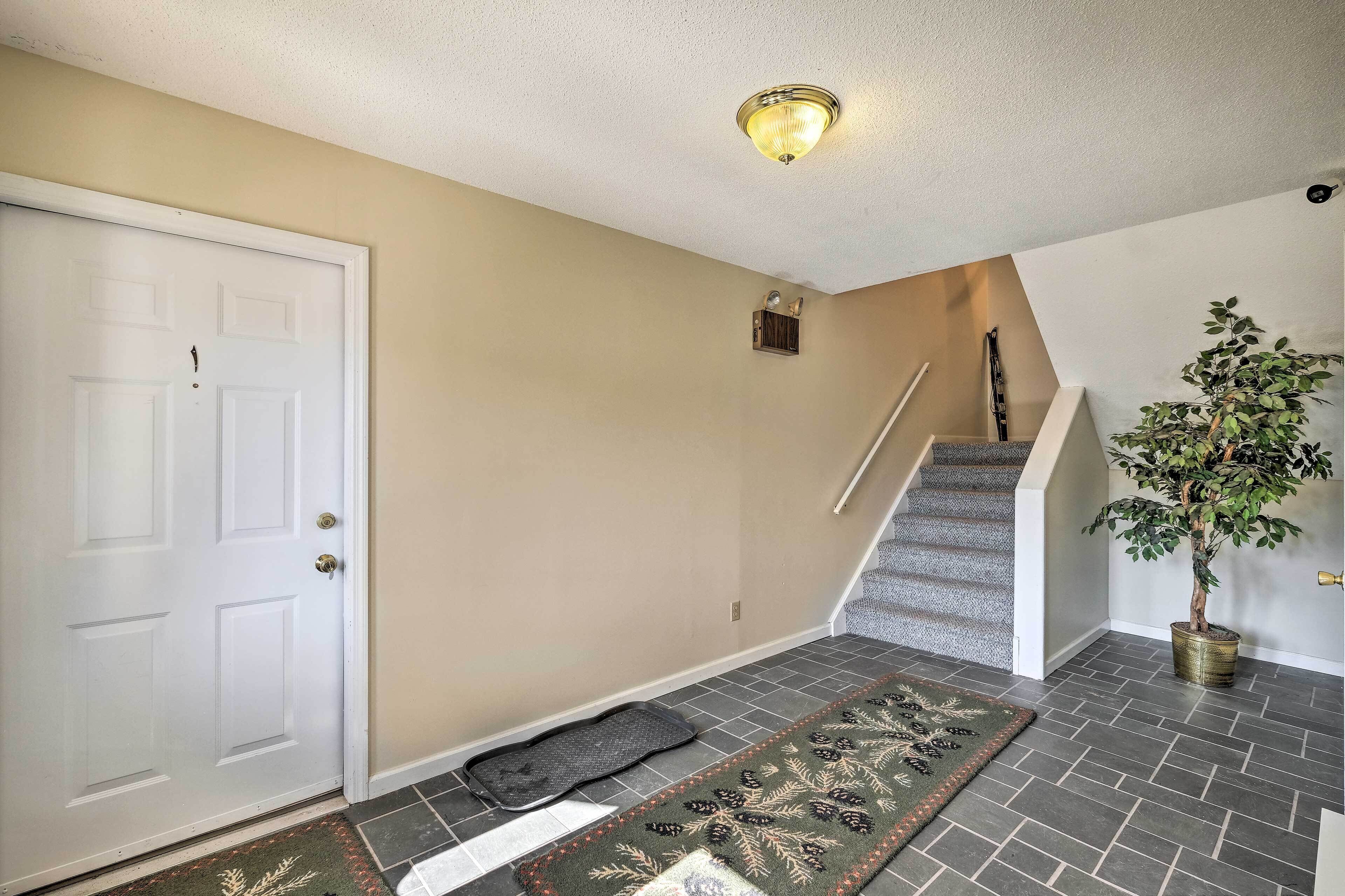A hallway with a white door, a staircase, a potted plant, and a patterned rug.
