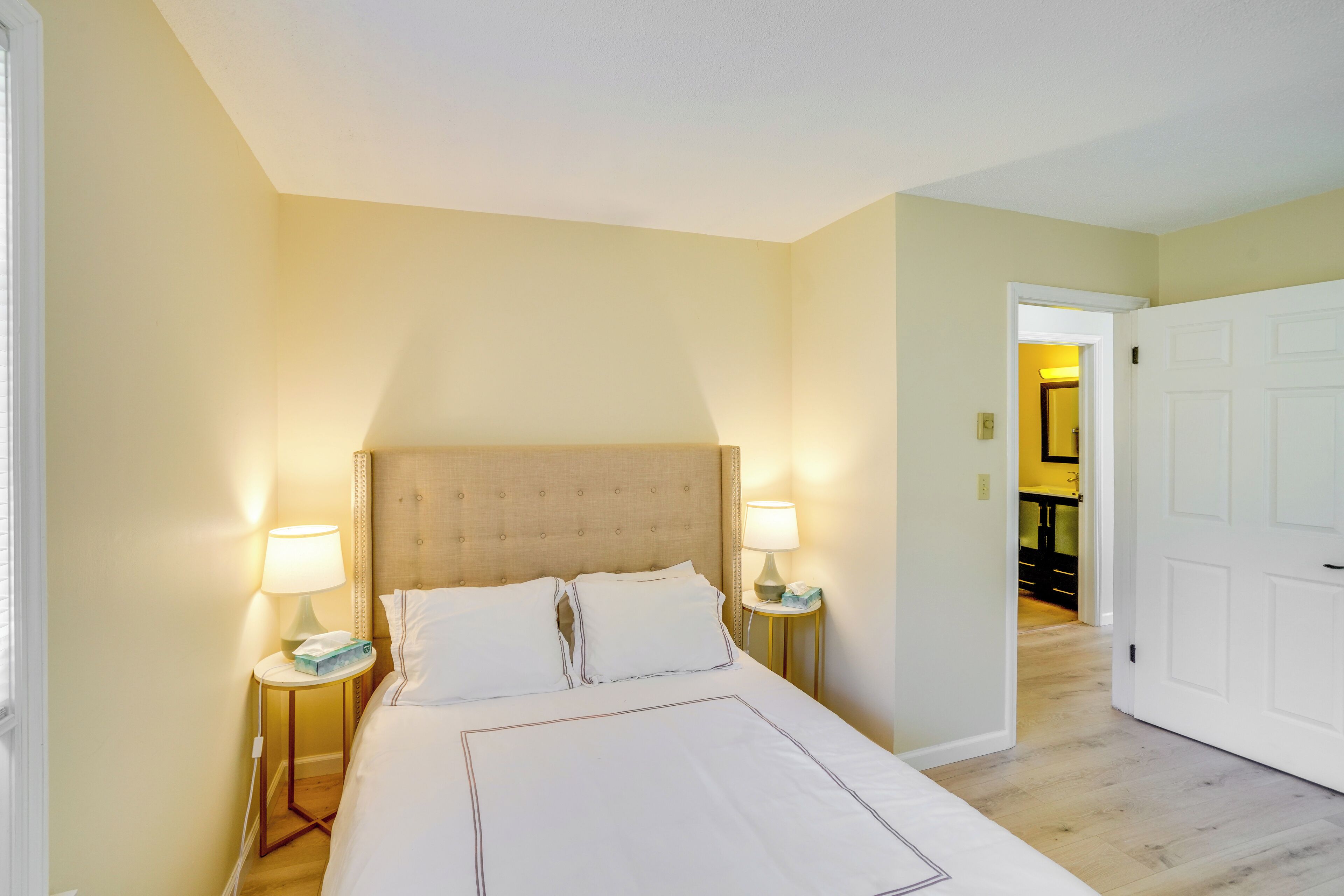 Une chambre d’hôtel avec un grand lit, deux tables de chevet avec des lampes, une tête de lit et une porte donnant sur un couloir.