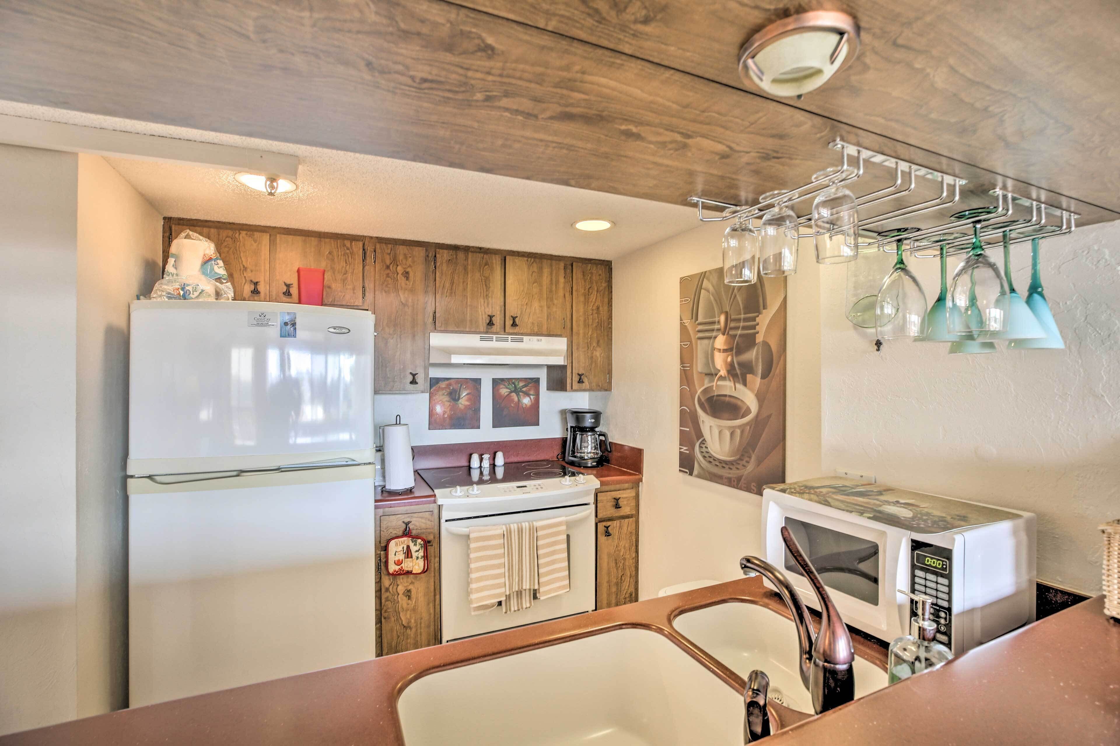 A compact kitchen with a refrigerator, stove, microwave, and a wine rack.