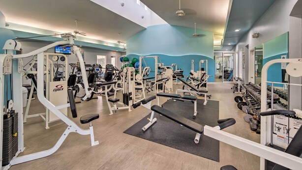 A gym with various exercise machines, a large mirror, and a ceiling fan. - Burnt Store Marina Condo: Boat, Swim, Golf! (Punta Gorda)