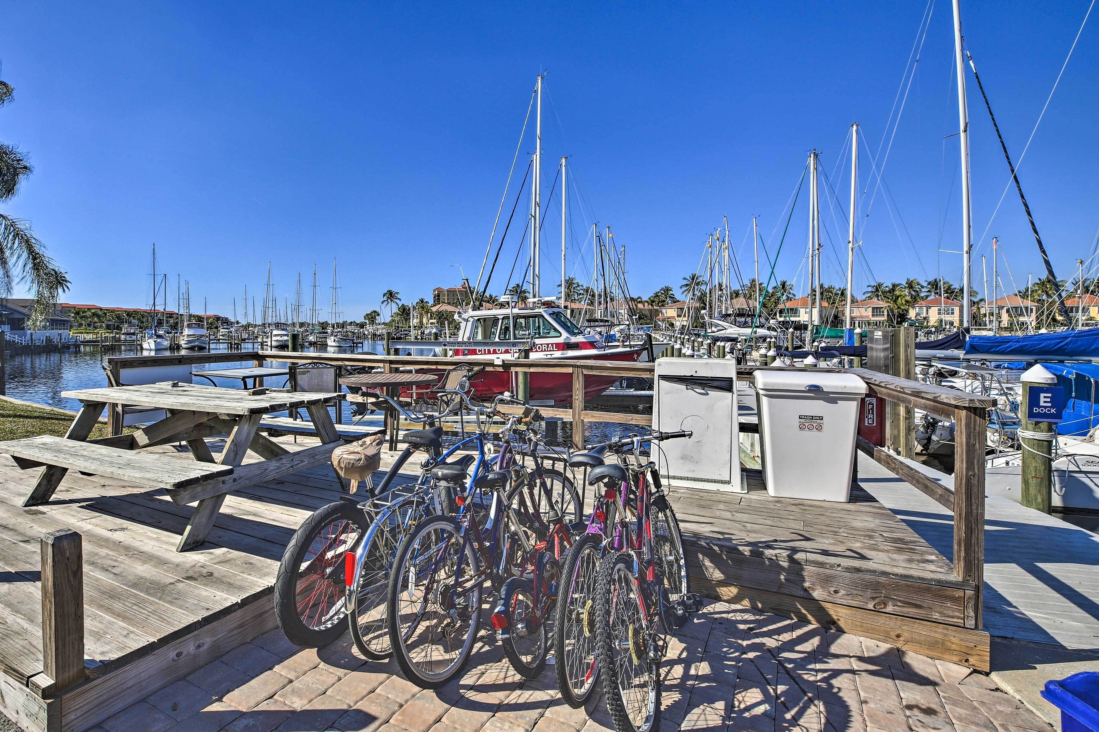 Un puerto deportivo con barcos amarrados, bicicletas y una terraza de madera con mesas de picnic.