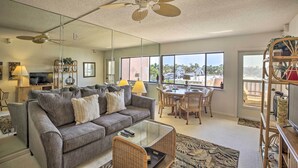 A living room with a grey sofa, a glass coffee table, a dining area with a table and chairs, a ceiling fan, and large windows offering a view of the outdoors. - Burnt Store Marina Condo: Boat, Swim, Golf! (Punta Gorda)