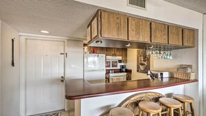 A kitchen with wooden cabinets, a stainless steel refrigerator, a microwave, and a bar area with stools. - Burnt Store Marina Condo: Boat, Swim, Golf! (Punta Gorda)