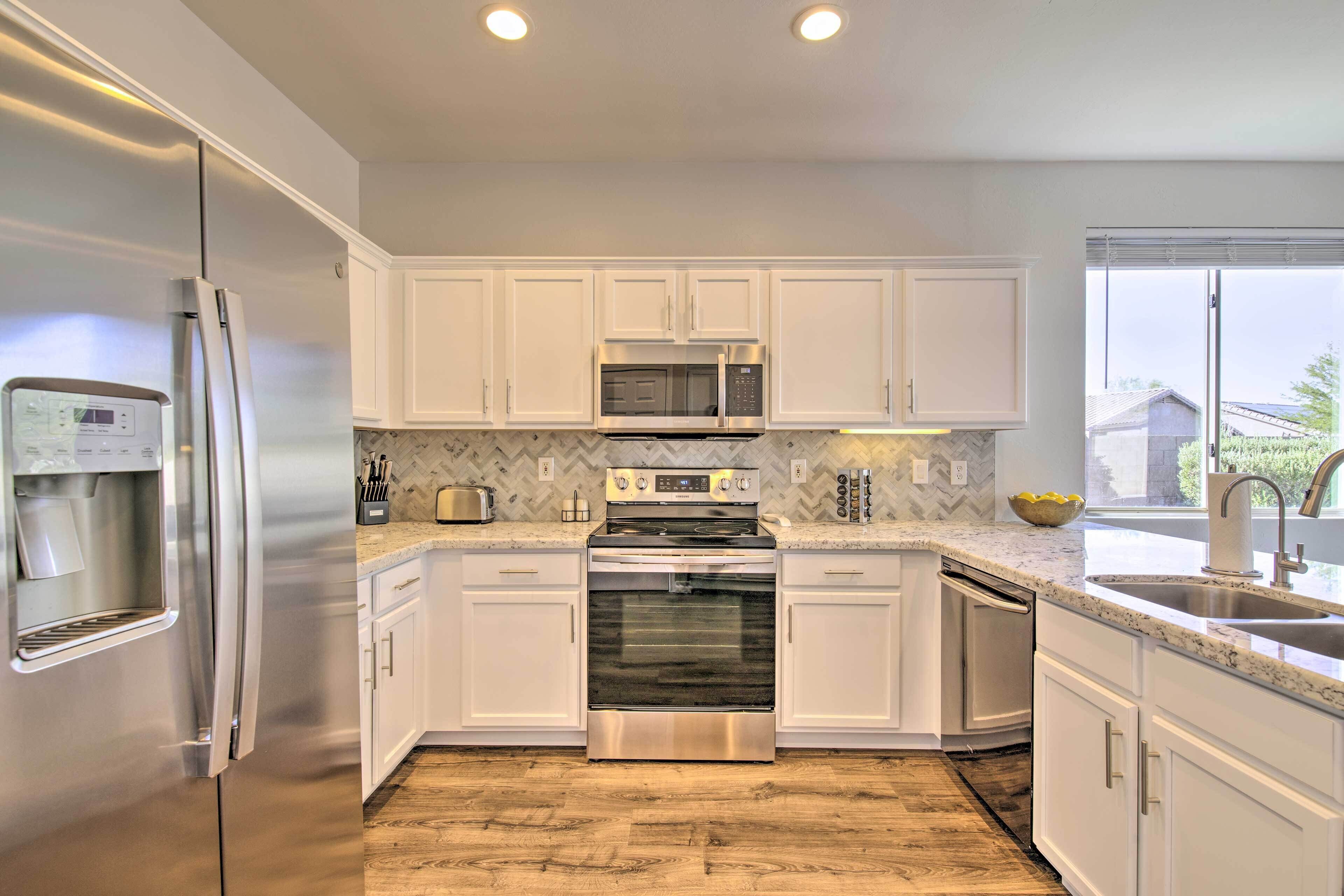 A modern kitchen with white cabinets, stainless steel appliances, a built-in oven, microwave, and dishwasher.