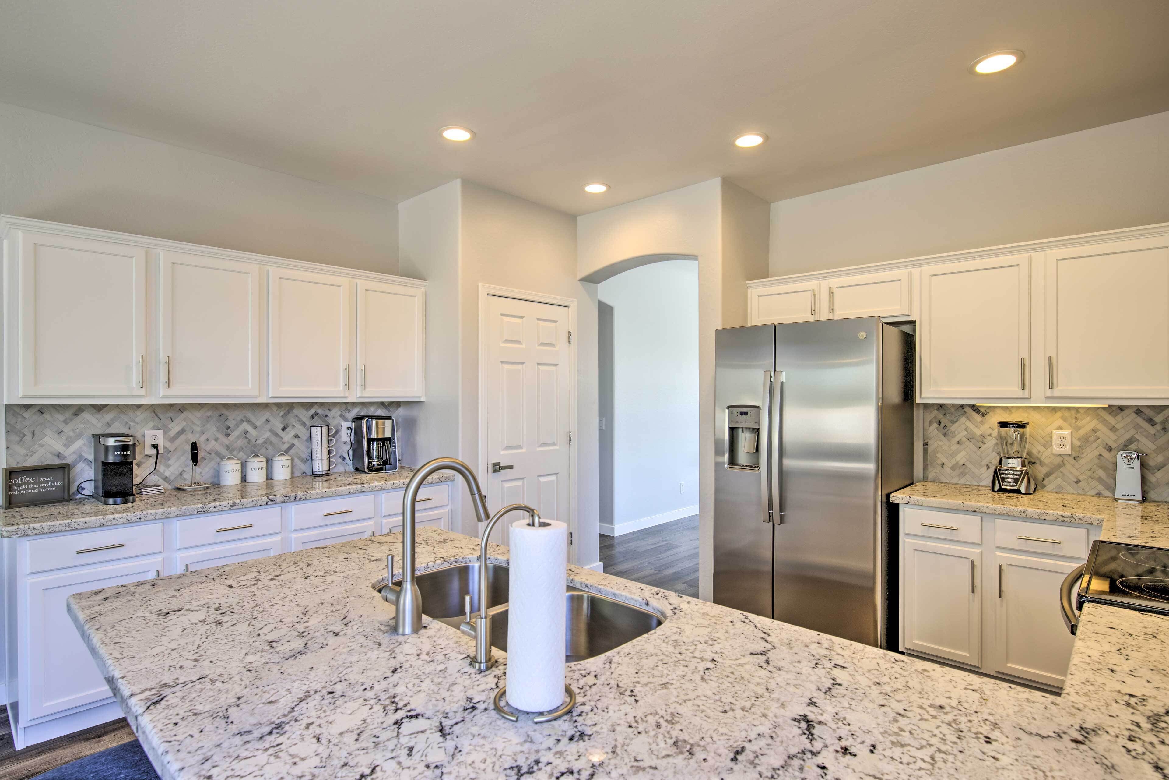 A modern kitchen with white cabinetry, granite countertops, stainless steel appliances, and a marble island.