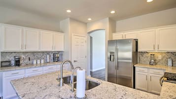 A modern kitchen with white cabinetry, granite countertops, stainless steel appliances, and a marble island.