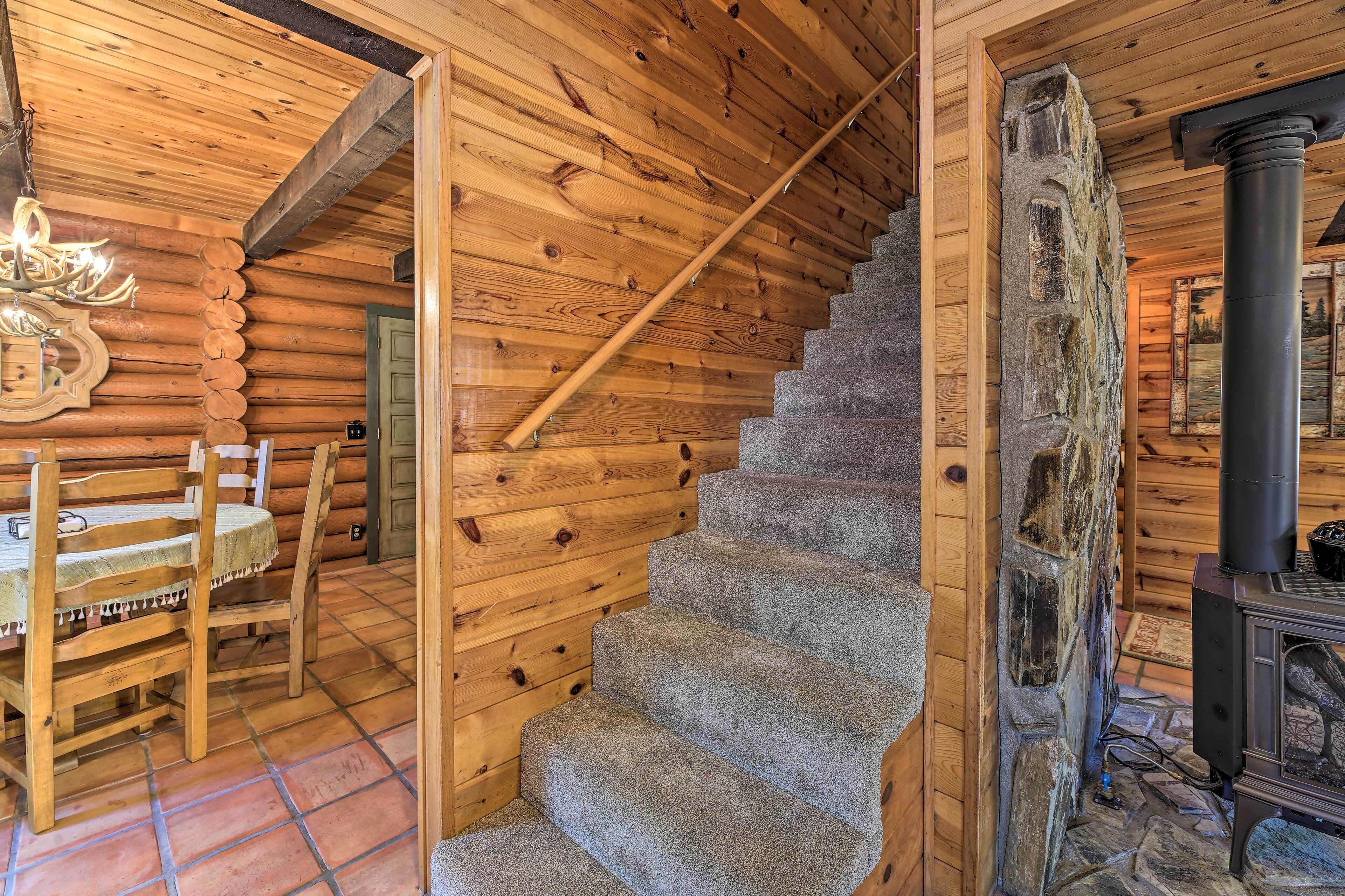 A wooden interior with a stone staircase, a dining area with a table and chairs, and a wood-burning stove.