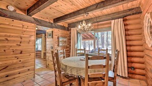 Ein Holzinterieur mit einem runden Tisch und Stühlen, einer Kandelaber und einem großen Fenster mit Vorhängen.