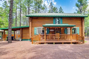 Eine Blockhütte mit Veranda und grünem Dach, umgeben von Bäumen.