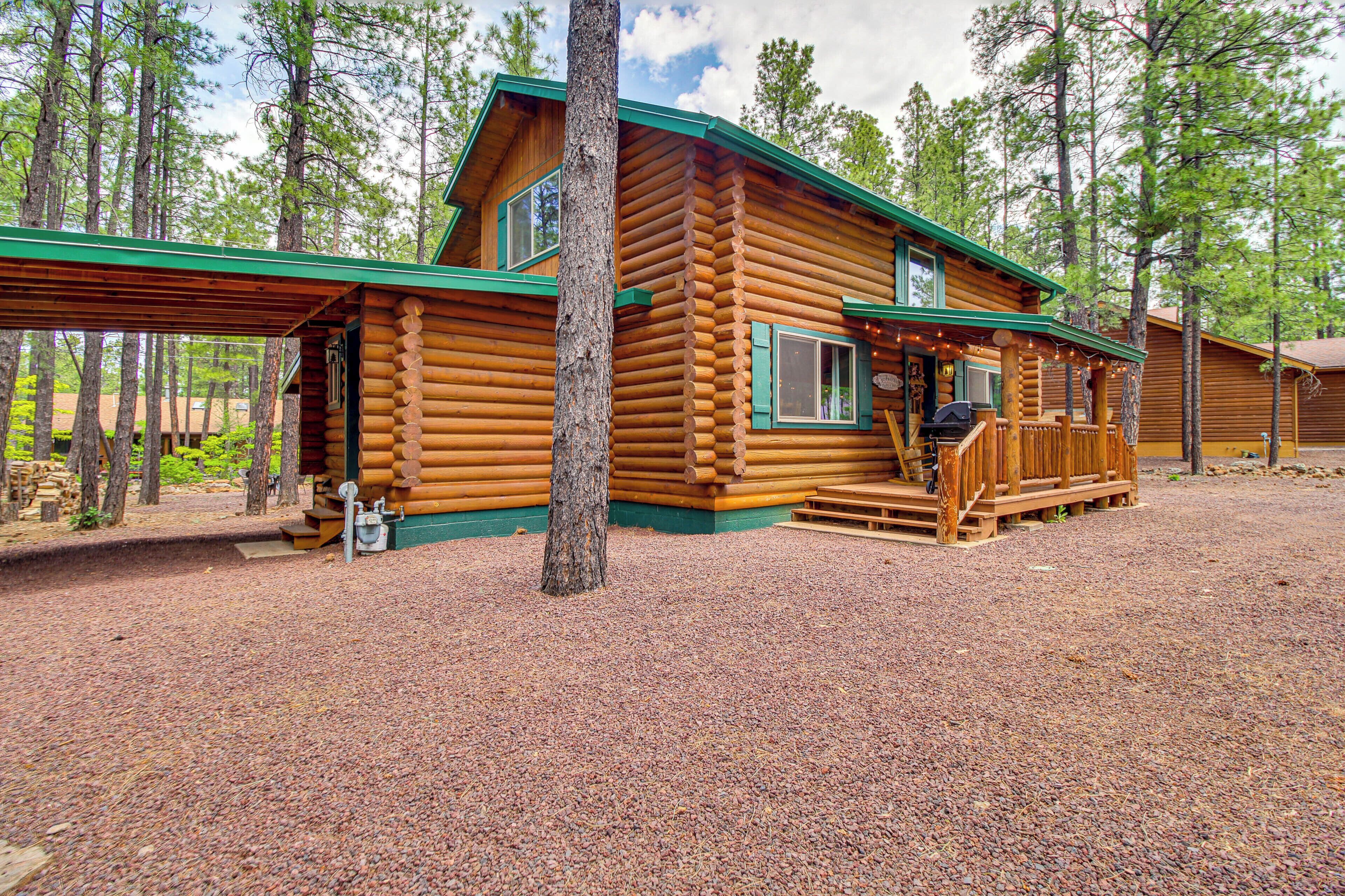 A log cabin with a porch, a grill area, and a view of the surrounding forest.