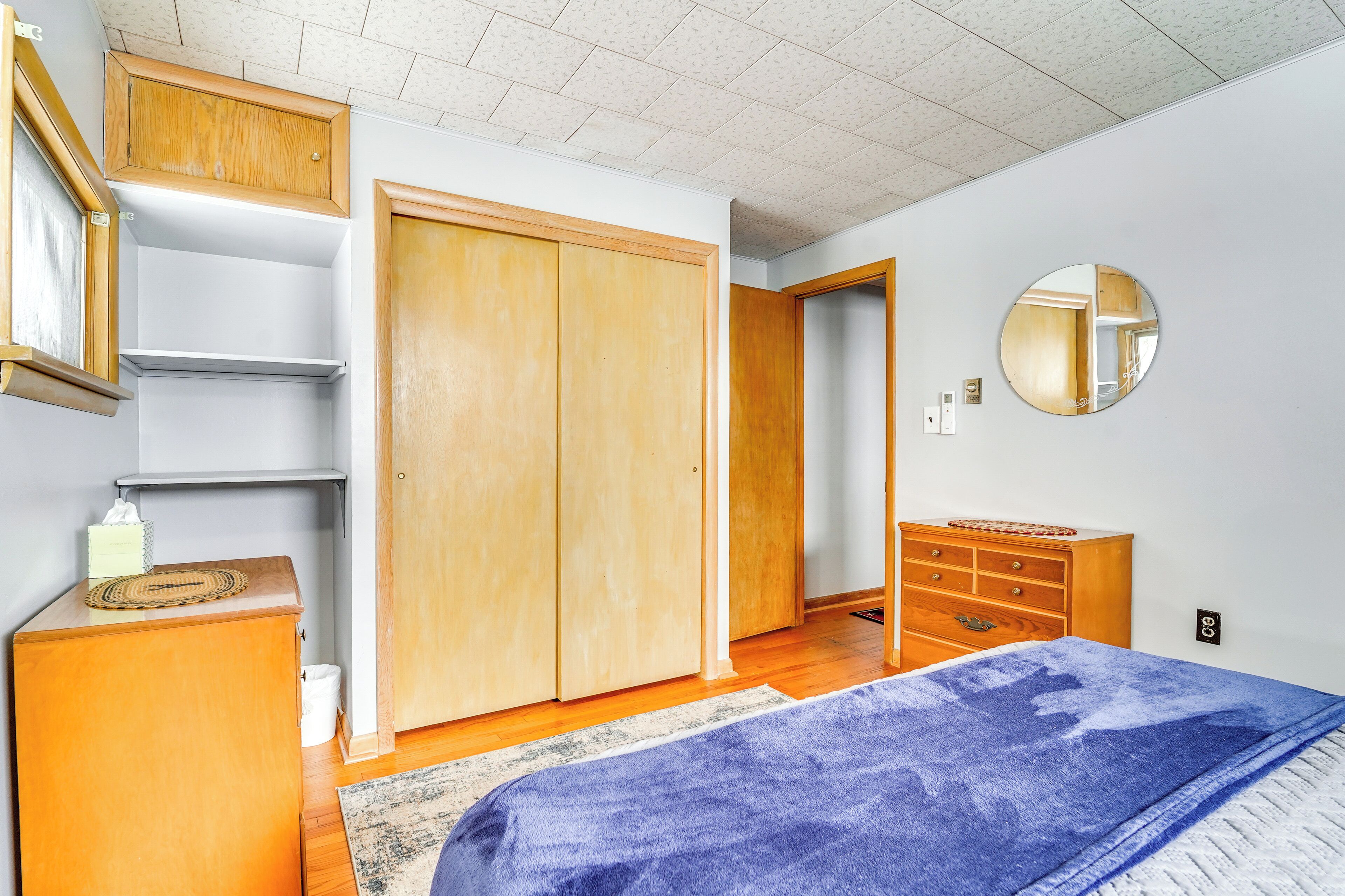 A bedroom with a bed, wooden wardrobe, dresser, and a mirror on the wall.