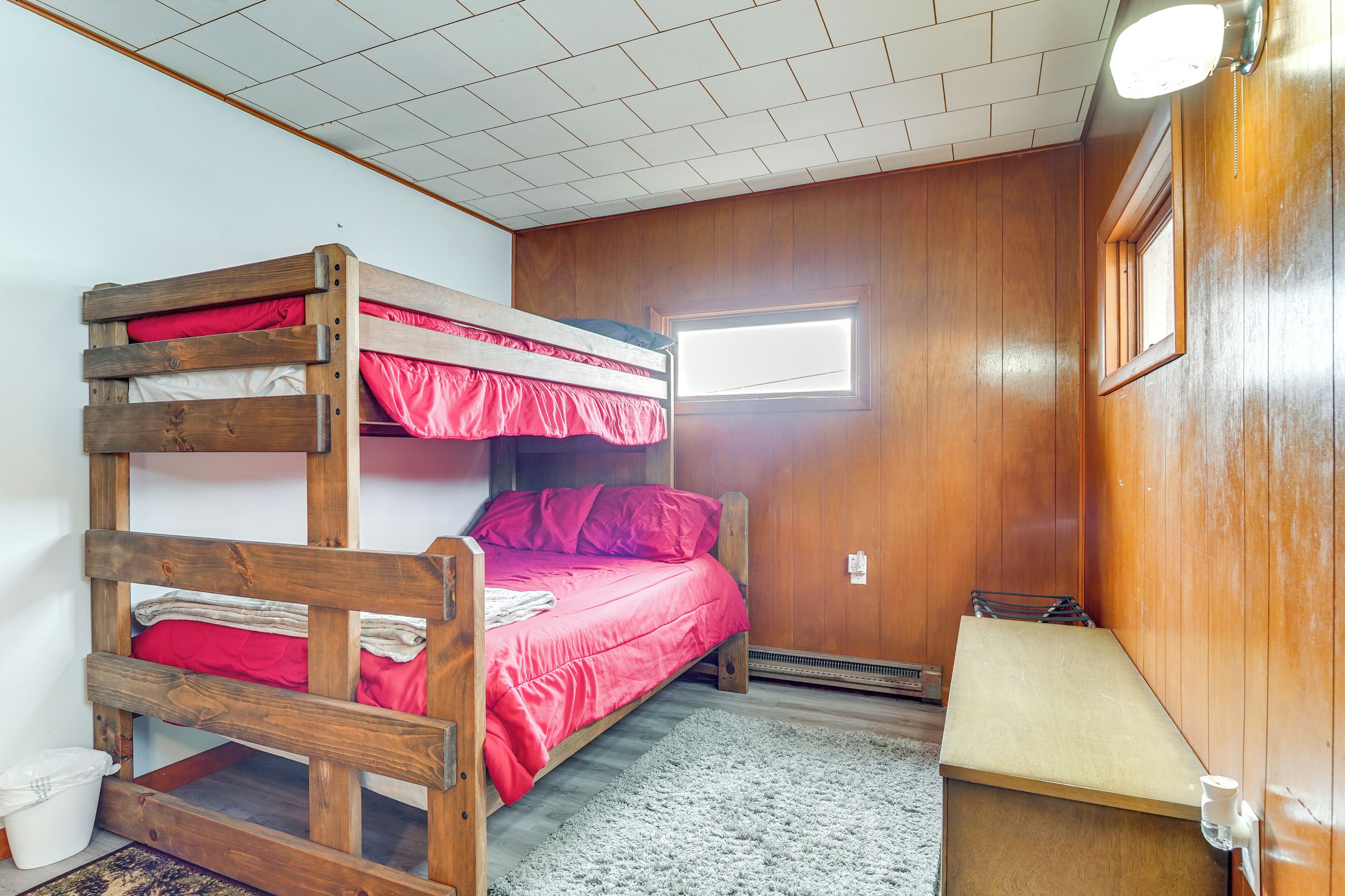 A bunk bed with red bedding, a small window, and a wooden wall.