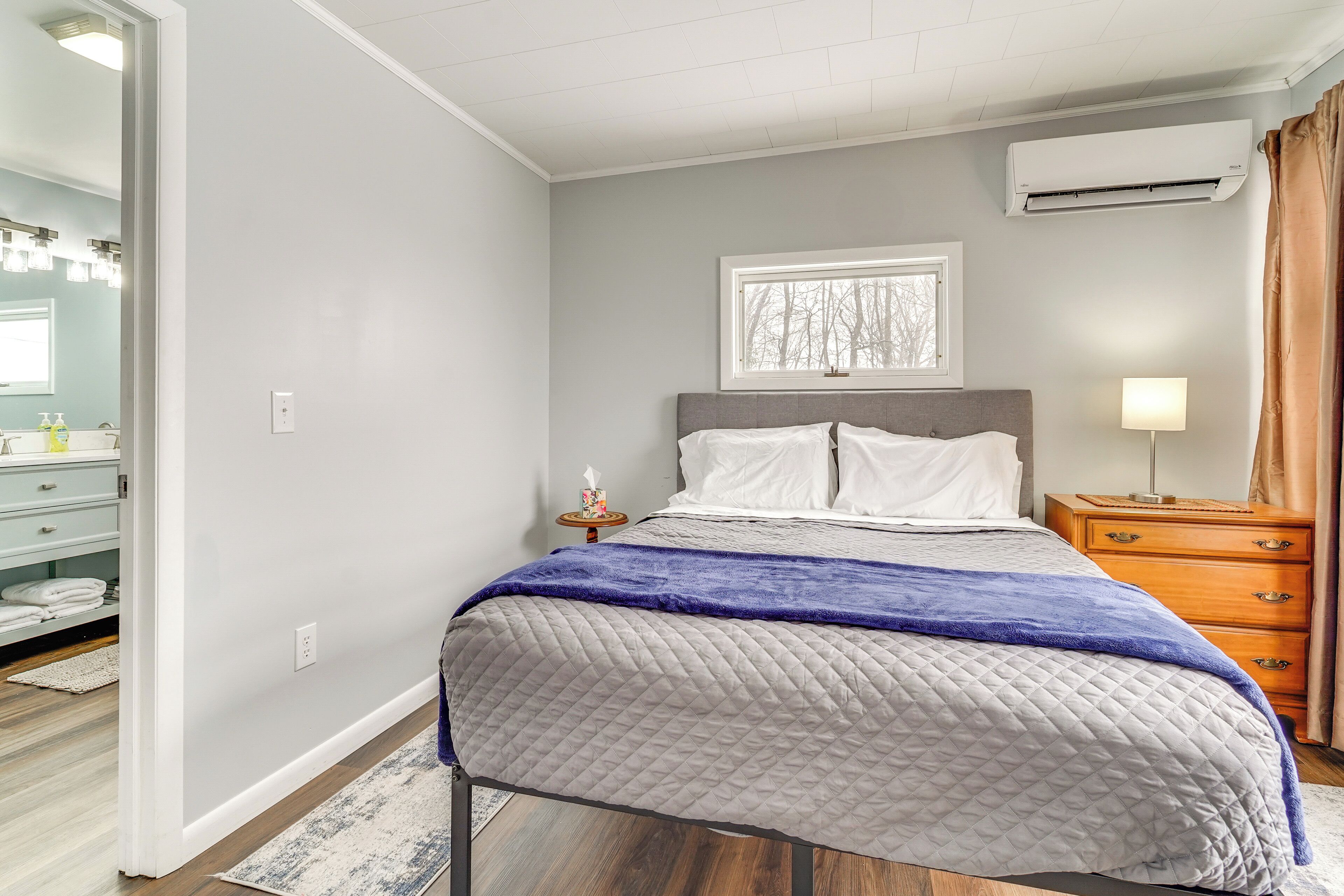 Un dormitorio con cama, mesita de noche, cómoda, ventana y aire acondicionado.
