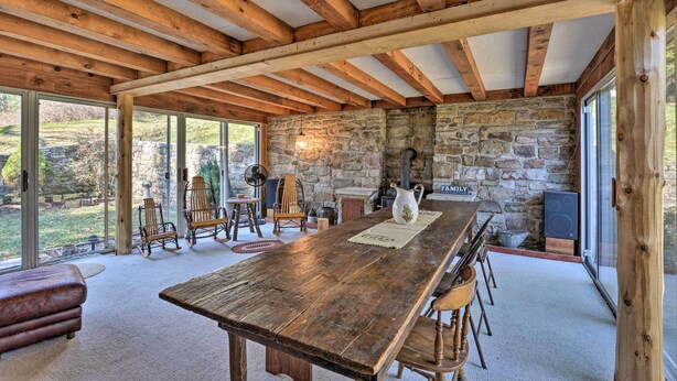 A rustic interior with a stone wall, wooden beams, a large wooden table, and a stone fireplace. - Cozy Home w/ Private Patio & Views, Hiking On-site (Belleville)