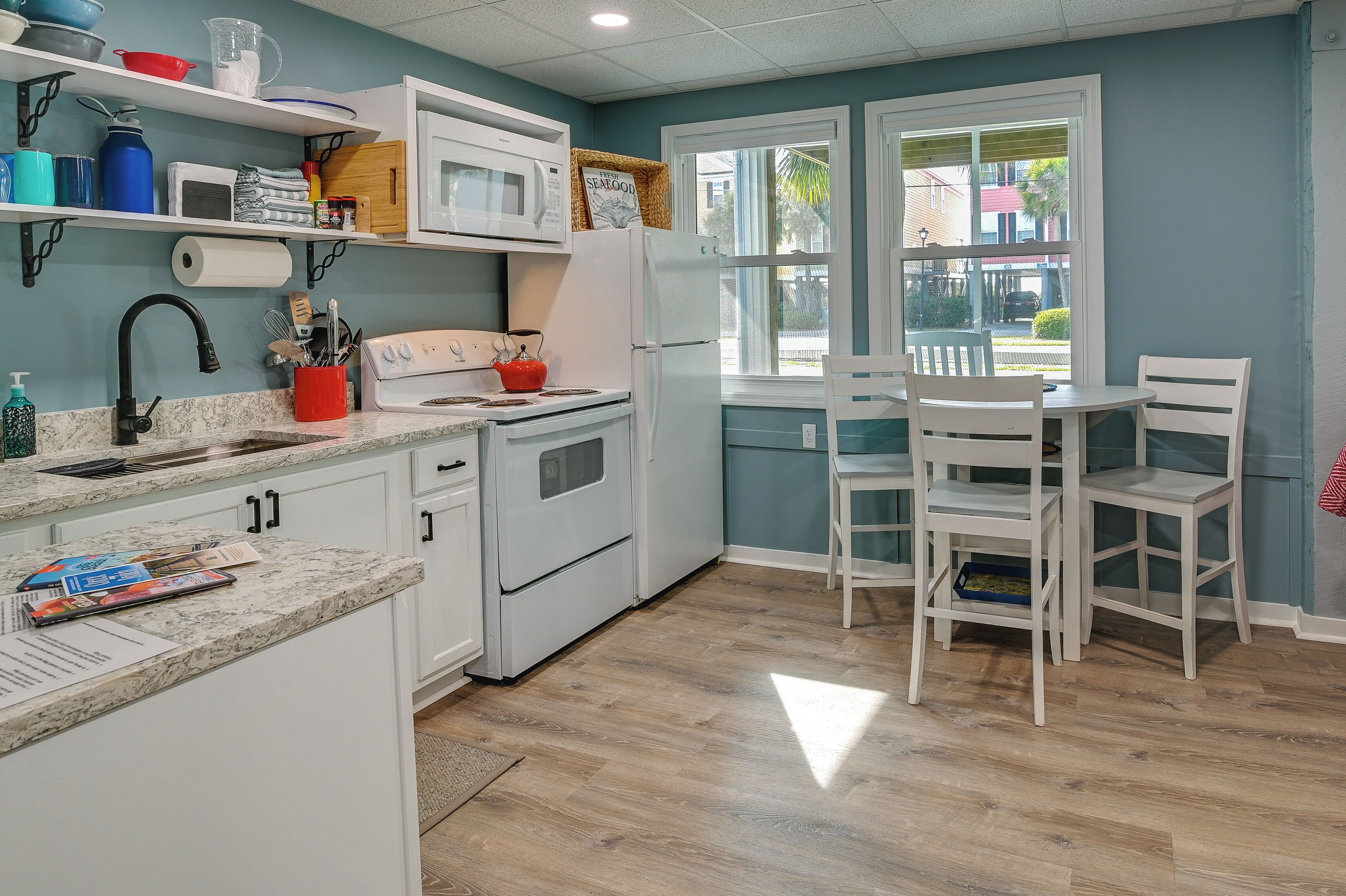 A compact kitchen with white appliances, a dining area with white chairs, and a window with a view of the outside.