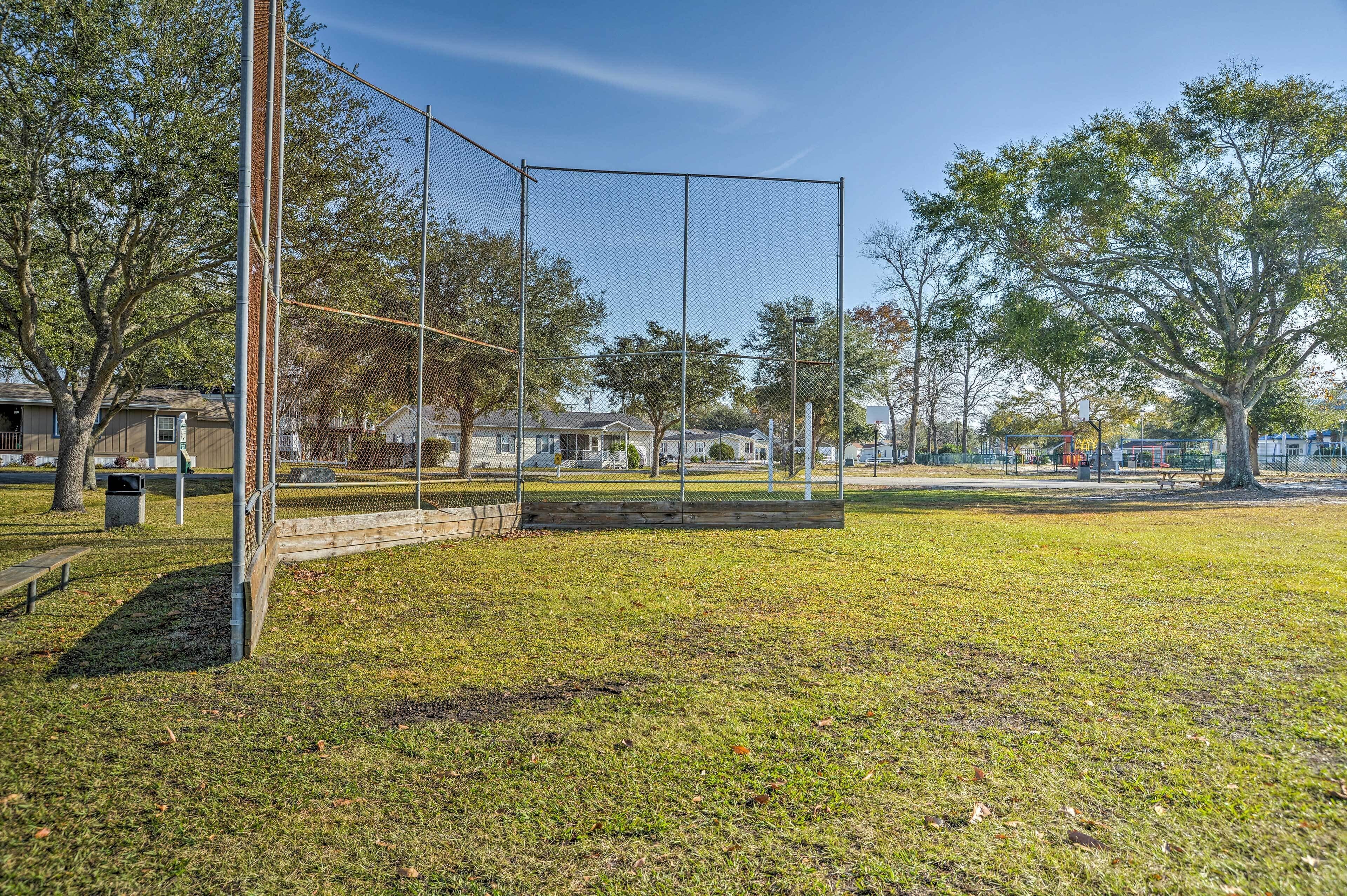 Una cancha deportiva cercada con un banco y árboles al fondo.
