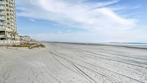 A beach with a building on the left, featuring multiple floors and balconies. - 'below Deck' Beach House: Walk to the Ocean! (Murrells Inlet)