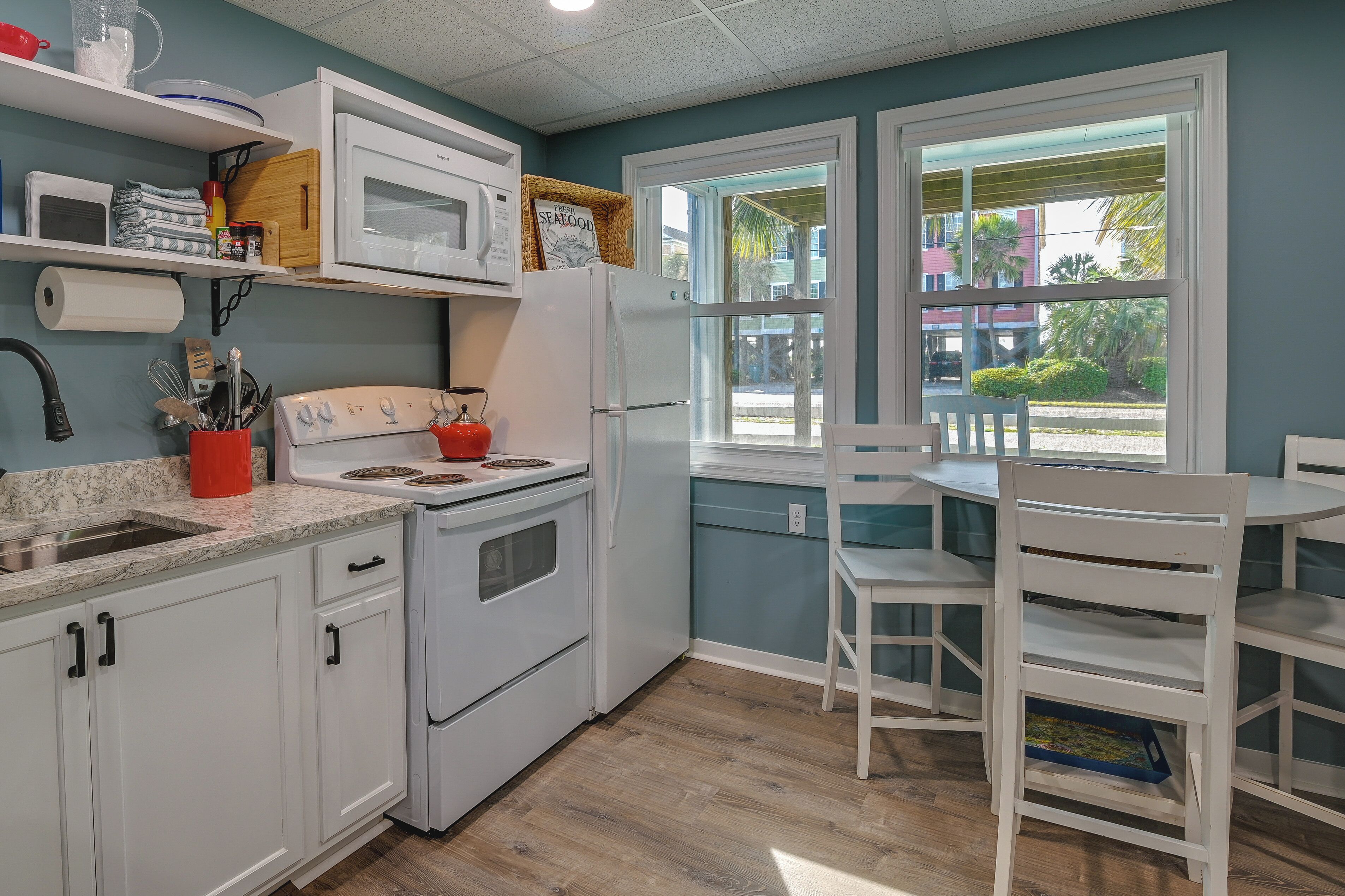 Una cocina con alacenas blancas, estufa, microondas y ventana con vista al exterior.