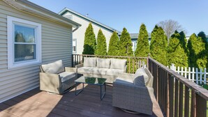A deck with wicker furniture, a glass table, and a white fence.