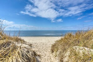 A beach path leading to the ocean with sand and grass on either side.