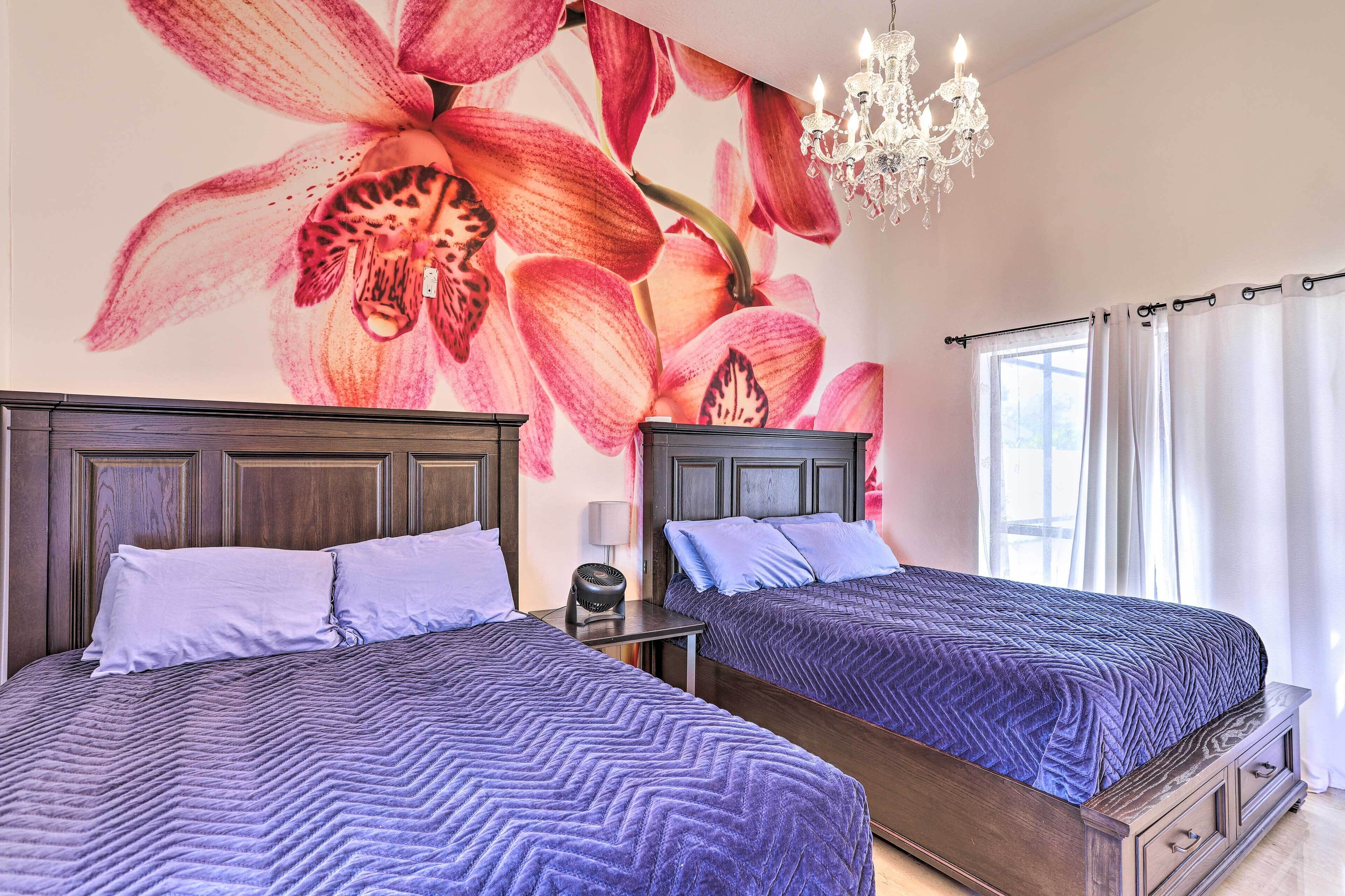 Une chambre avec deux lits, un lustre et une fresque murale à motifs floraux.